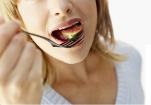 Portrait of young woman eating a sliced fig with a fork